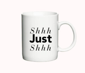 Hvid kaffekop med teksten "Shhh Just Shhh" i en kombination af kursiv og fed skrifttype.