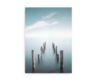 Plakat med en træmole af nedbrudte pæle, der strækker sig ud i et roligt hav under en klar, blå himmel.