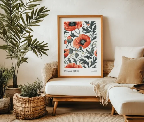 William Morris Poppy Garden plakat med røde valmuer og grønt løv, indrammet og stående på en sofa i en hyggelig stue.