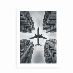 Sort-hvid kunstplakat med et fly, der passerer mellem høje bygninger set i dramatisk perspektiv.