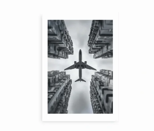 Sort-hvid kunstplakat med et fly, der passerer mellem høje bygninger set i dramatisk perspektiv.