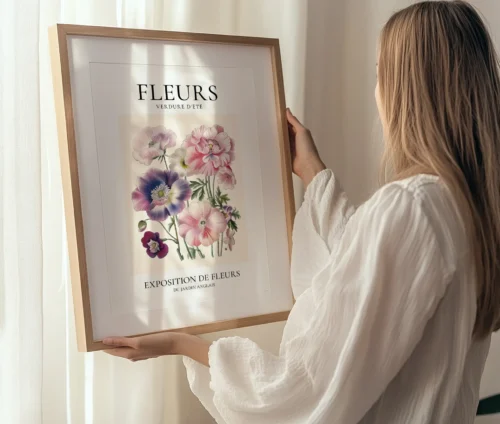 Kvinde holder en indrammet plakat med blomsterillustrationer og teksten "Fleurs – Verdure d'Été".