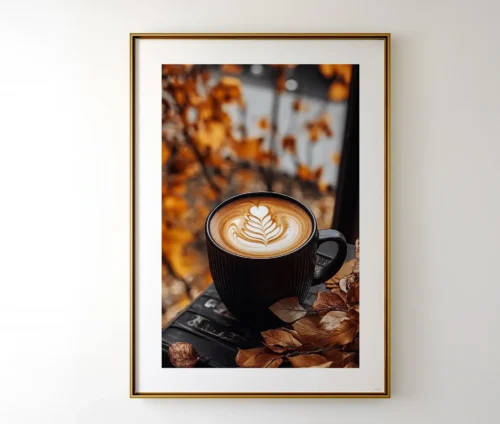 Indrammet kaffeplakat med mørk kop og latte art omgivet af efterårsblade på væg.