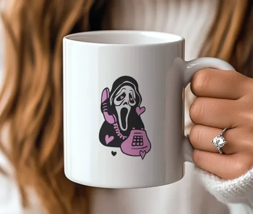 En person holder et hvidt krus med et sjovt Scream-motiv og lilla detaljer.
