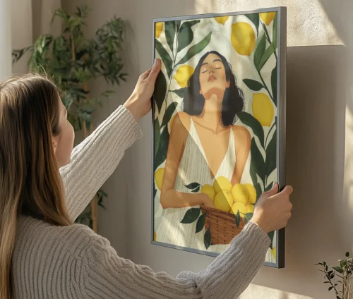Person hænger en kunstplakat med citrusfrugter og en kvinde op på en væg.
