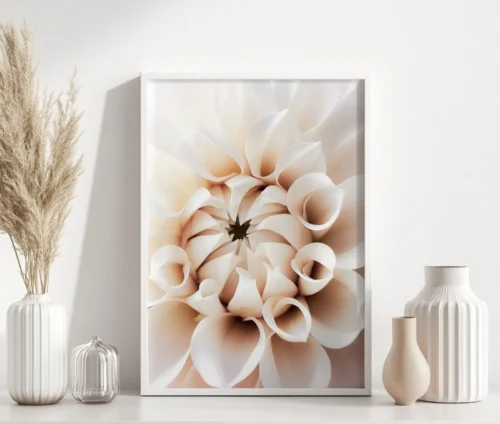 Plakat med et nærbillede af en beige dahlia i en hvid ramme, placeret på en hvid overflade med stilrene dekorationer.
