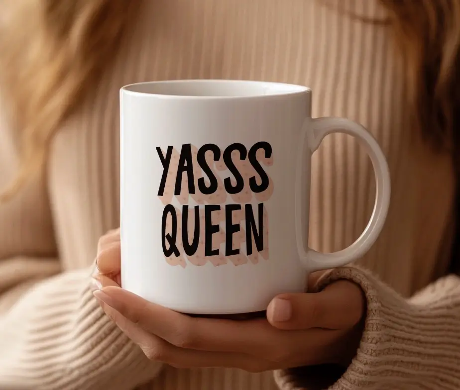 Hvidt kaffekrus med teksten Yasss Queen i en fed, sort skrifttype med lyserød skyggeeffekt.