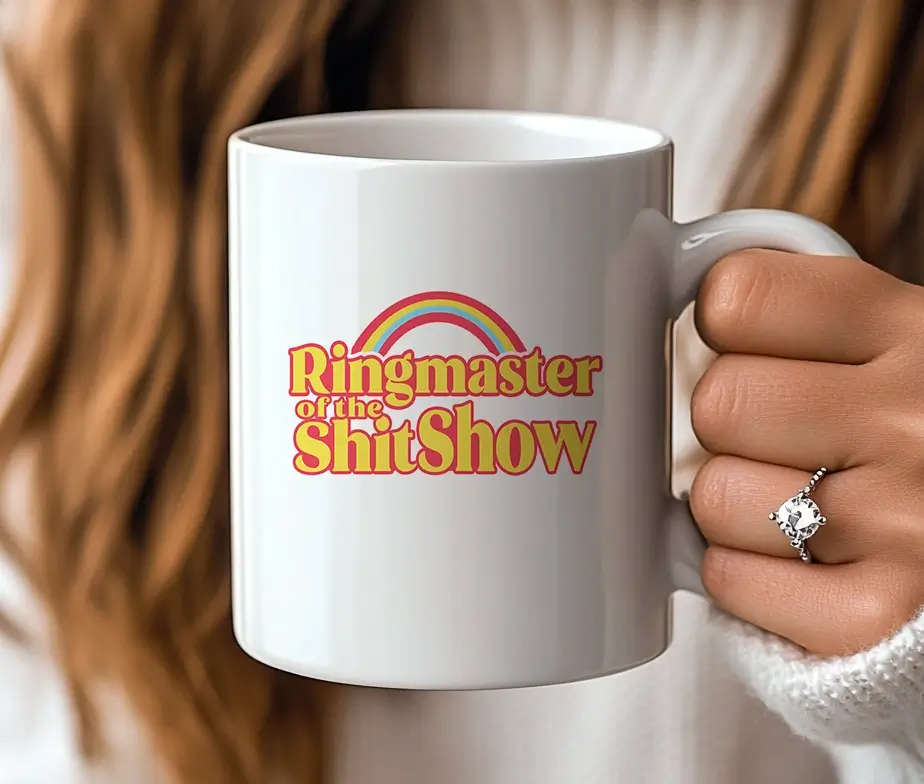En person holder et hvidt krus med teksten "Ringmaster of the ShitShow" i retro-design.