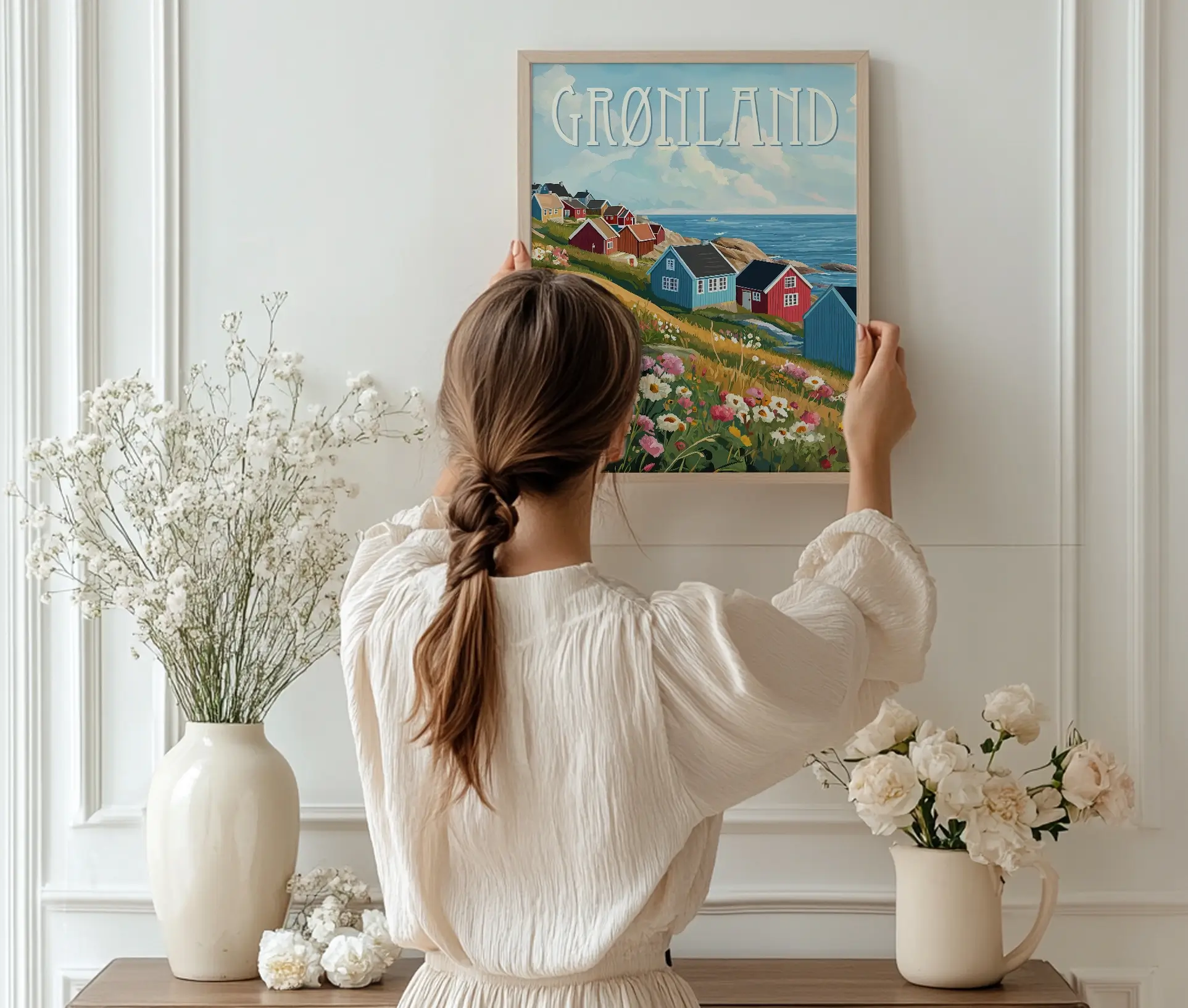 Kvinde hænger plakat op med grønlandske kysthuse og blomster