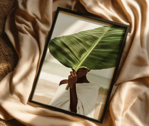 Plakat med kvinde og bananblad i sort ramme liggende på beige tekstiler