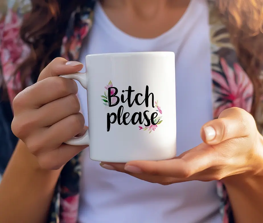 Krus med teksten "Bitch Please" og blomsterdetaljer holdt i hænder