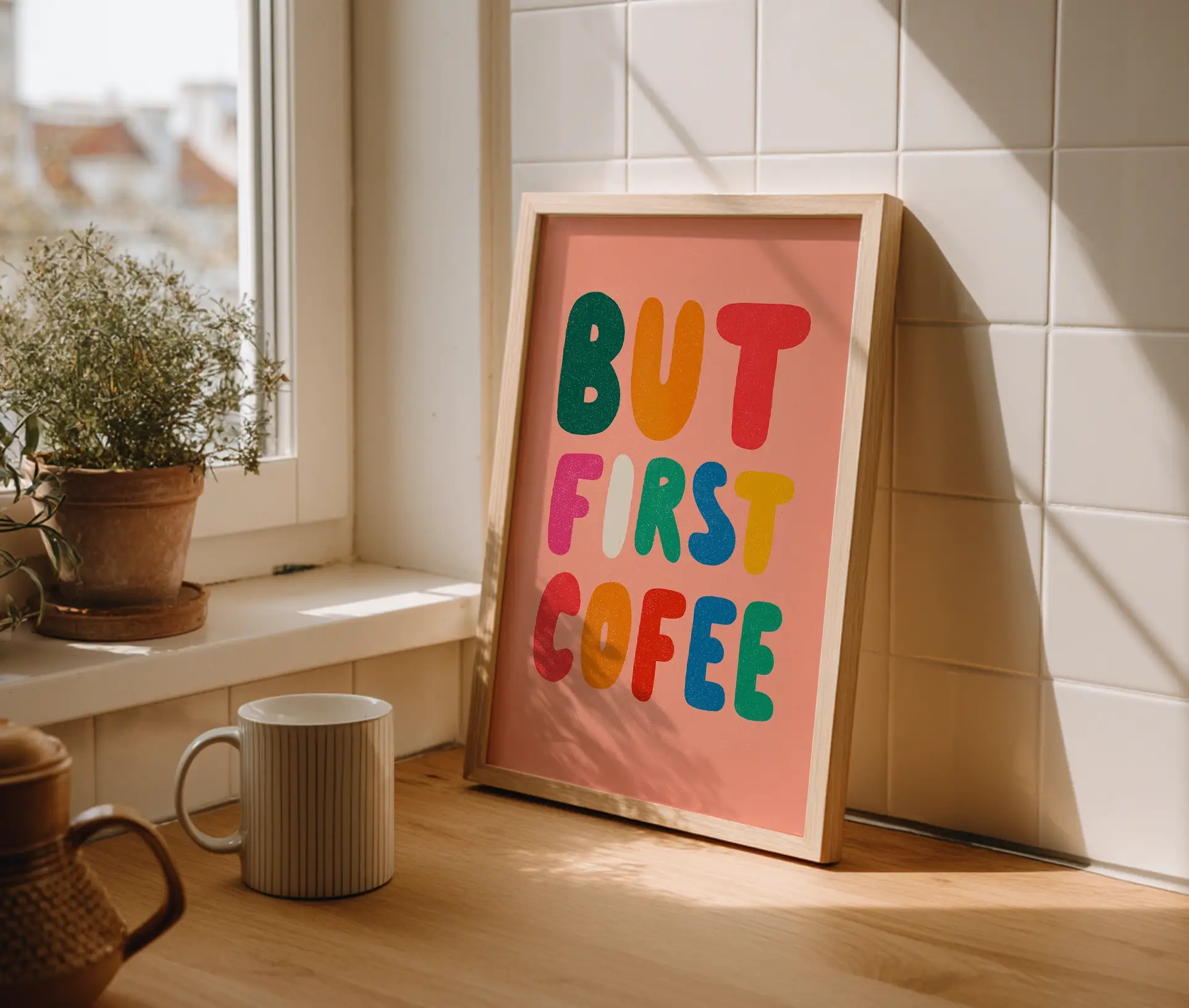 Plakat med teksten But First Coffee i farverige bogstaver, placeret på køkkenbord