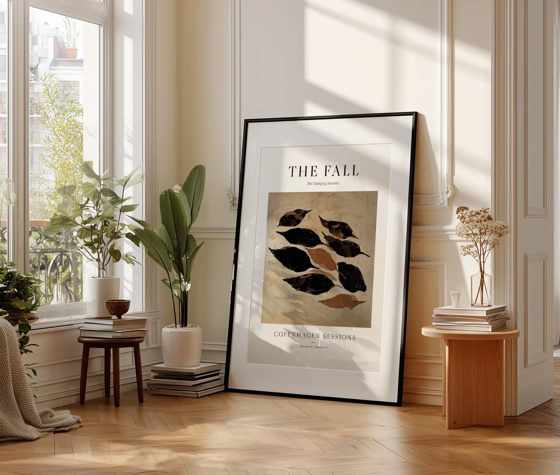 Stor plakat med abstrakte efterårsblade i ramme, stående i sollys i stue med planter og bøger.