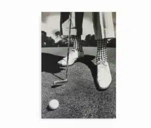 Sort/hvid plakat med golfmotiv. Nærbillede af golfsko, tjekkede sokker og golfkølle klar til slag.