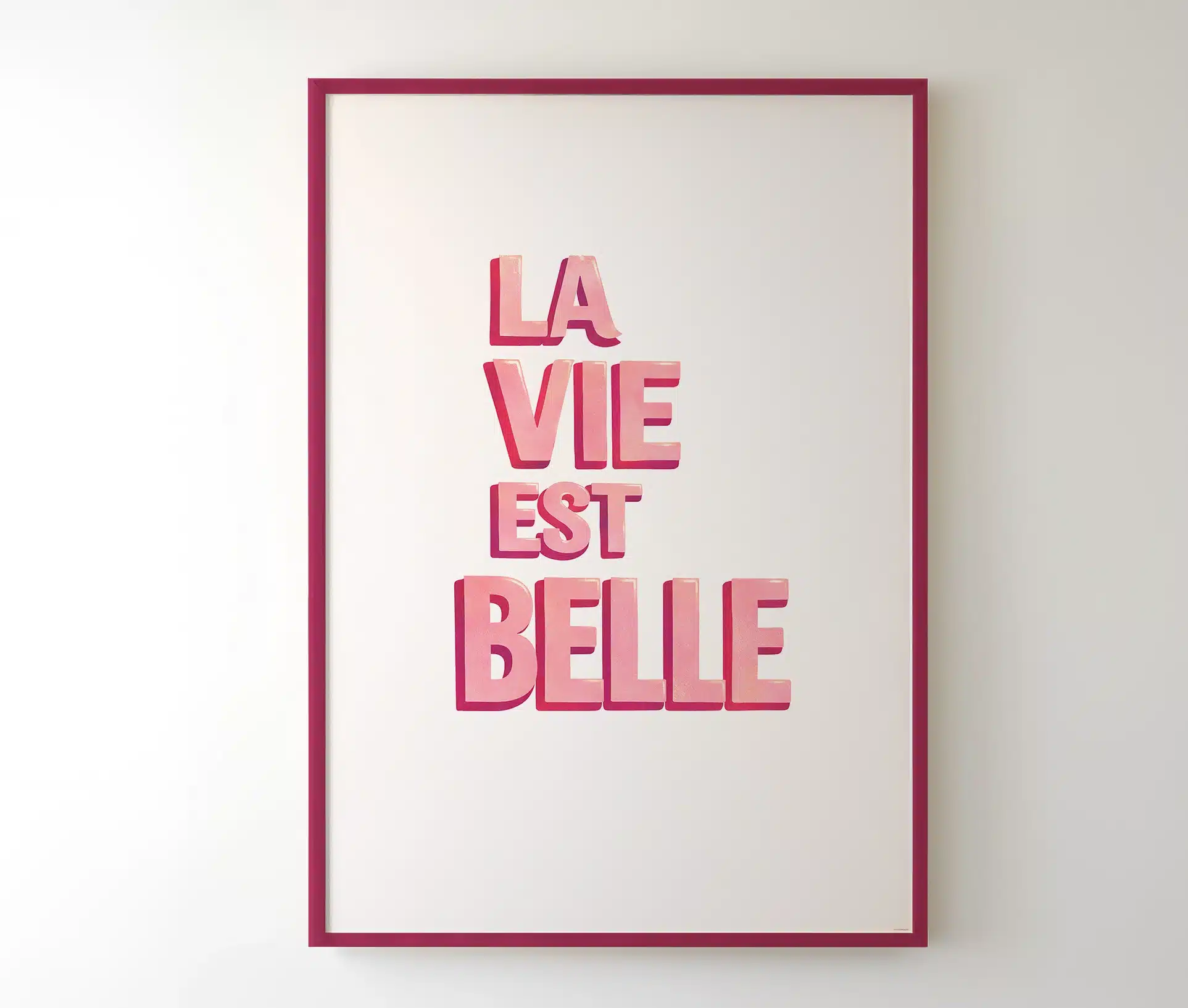 La Vie Est Belle plakat i mørk pink ramme på hvid væg
