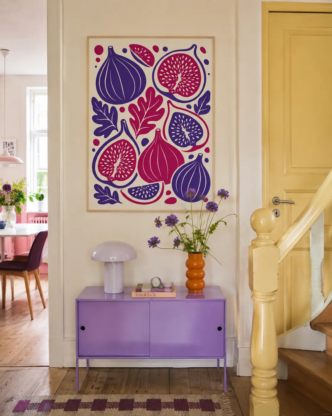 Figenplakat ophængt i farverig entré over lilla skænk med orange vase og blomster